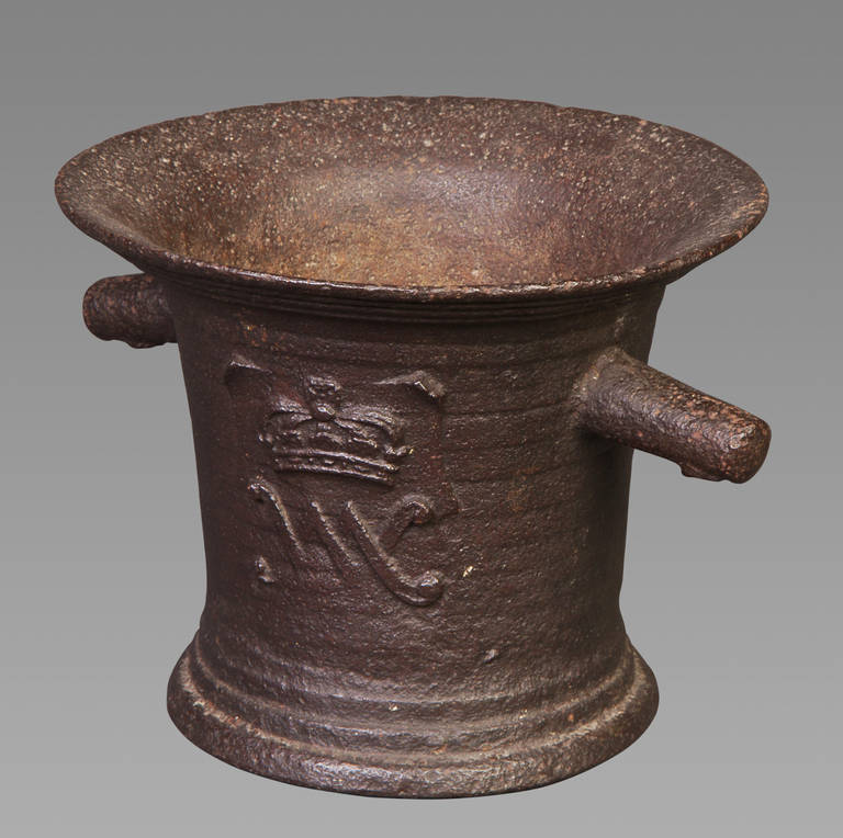 A late 17th century iron mortar of large proportions with sharply everted rim and corded, slightly tapering sides, with two lug handles, cast to either side with the cipher 'VM' beneath a crown for William and Mary, on a spreading moulded foot.