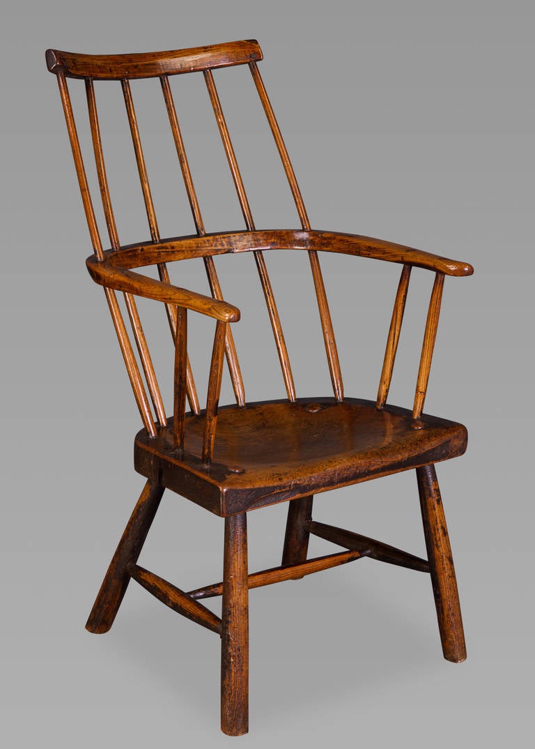 With a curved comb back encompassing a horseshoe shaped armrest above a thick saddle-shaped elm slab seat over four legs joined by an H-stretcher. The chair is completely original and retains vestiges of the original paint. This chair has everything