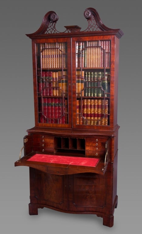 Of compact form with swan’s neck pediment terminating in foliate roundels framing a bust-plinth and finely carved fretwork panel. The upper case with a pair of glazed astragal 15 panel doors enclosing adjustable bookshelves. The lower case of