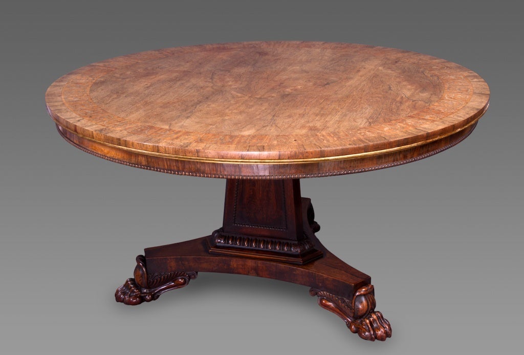 The circular tilt top of beautiful naturally faded goncalo alves inlaid with a wide marquetry band of fruiting vines above an elegant parcel gilt and bead molded  shallow frieze, the panelled triform columnar support decorated with marquetry