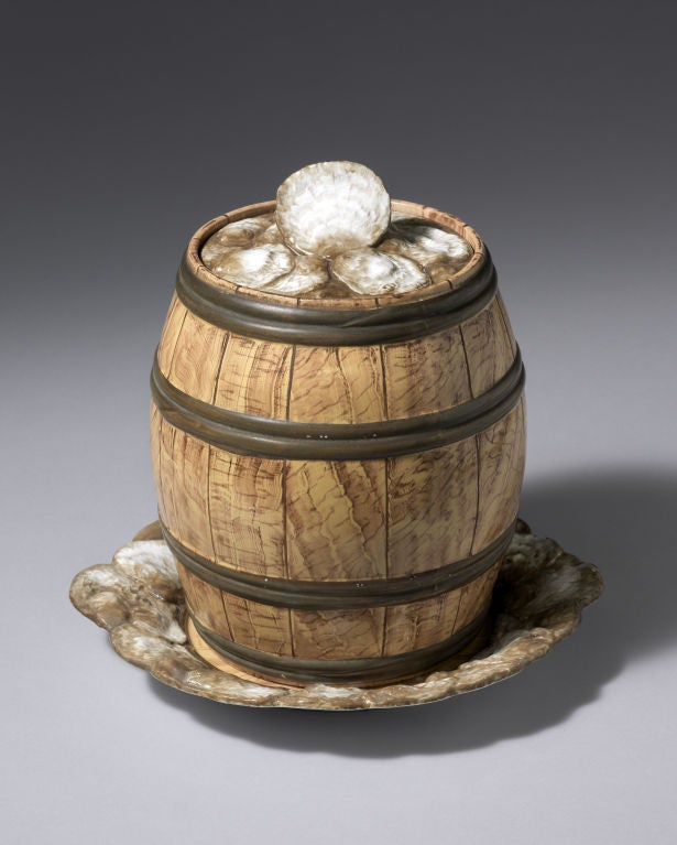 A Wedgwood Pearlware Trompe L’Oeil Oyster Barrel, Cover and Stand, the stand and barrel painted as faux bois with darker iron banding to the barrel, the edge of the stand and the cover moulded and painted to simulate oysters.<br />
<br />
Mark: