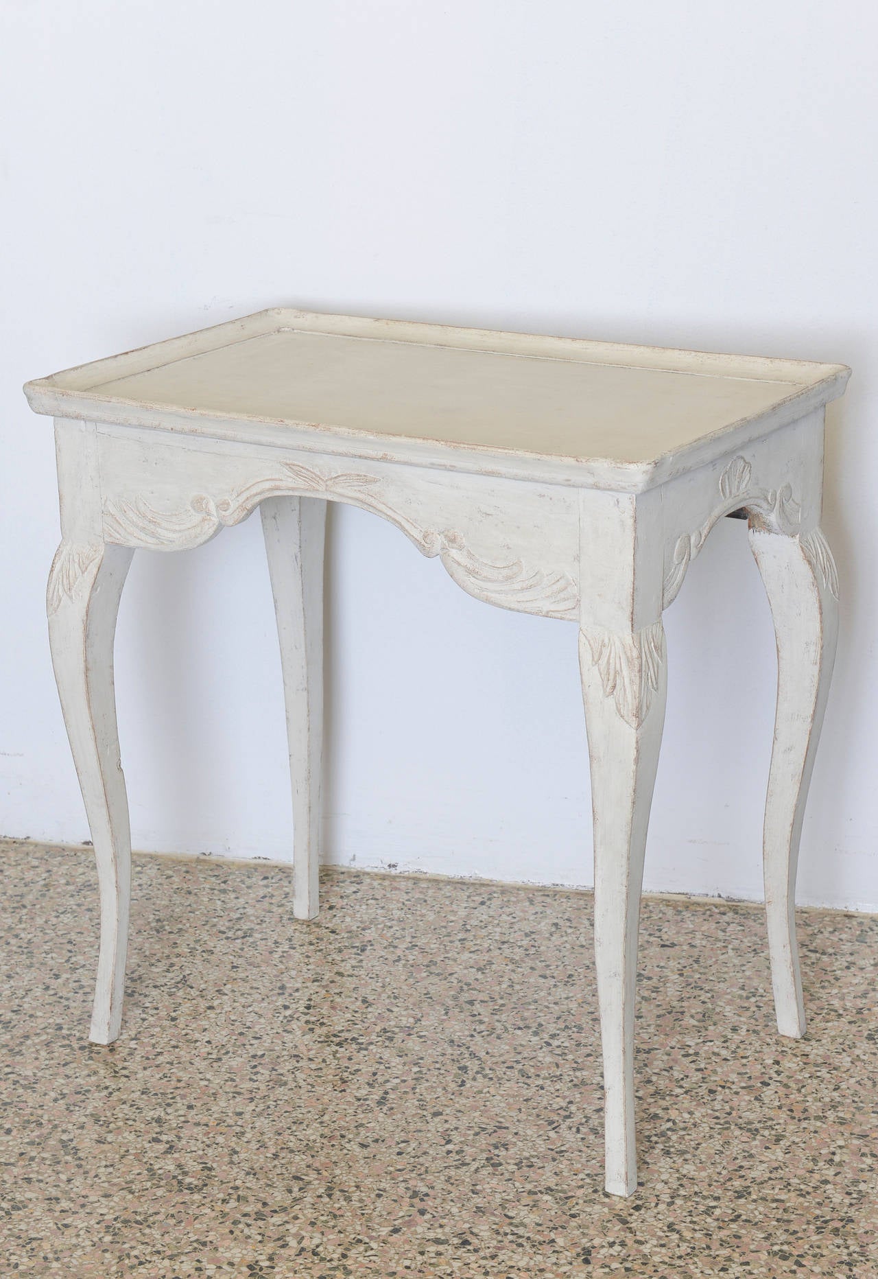 Late 18th Century Antique Swedish Gustavian Table. This lovely table has graceful cabriole legs and a framed top. The curved apron is carved in a shell and acanthus leaf motif. The paint is refreshed in a light grey-white distressed wash.

28.50 in