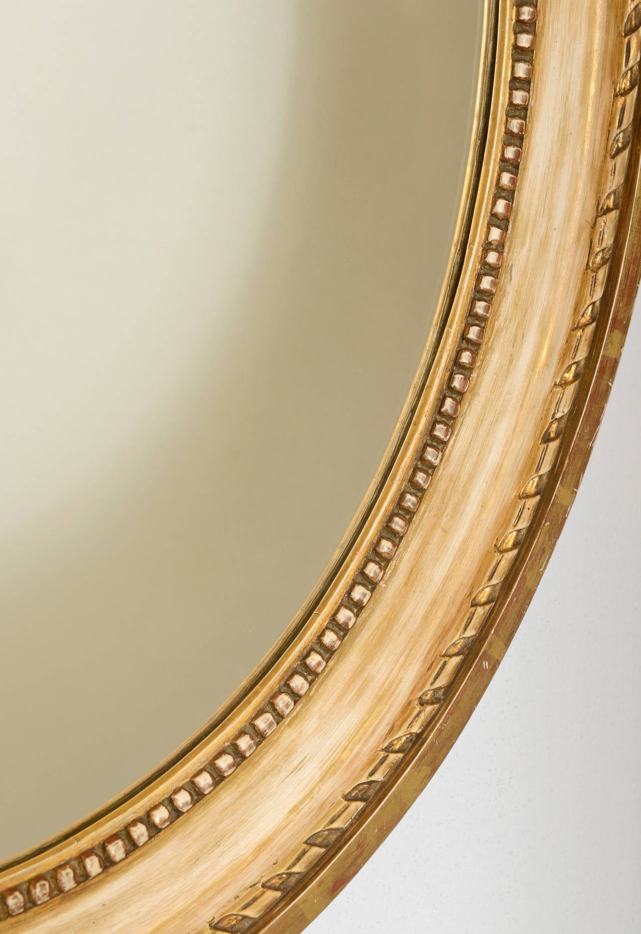 Pair of Swedish Antique Mirrors. Two beautiful antique mirrors in a classic oval shape. The frame is carved in a beaded and grooved pattern around the perimeter. They are painted a beige-white-gold-tone refreshed paint with gilded edges.