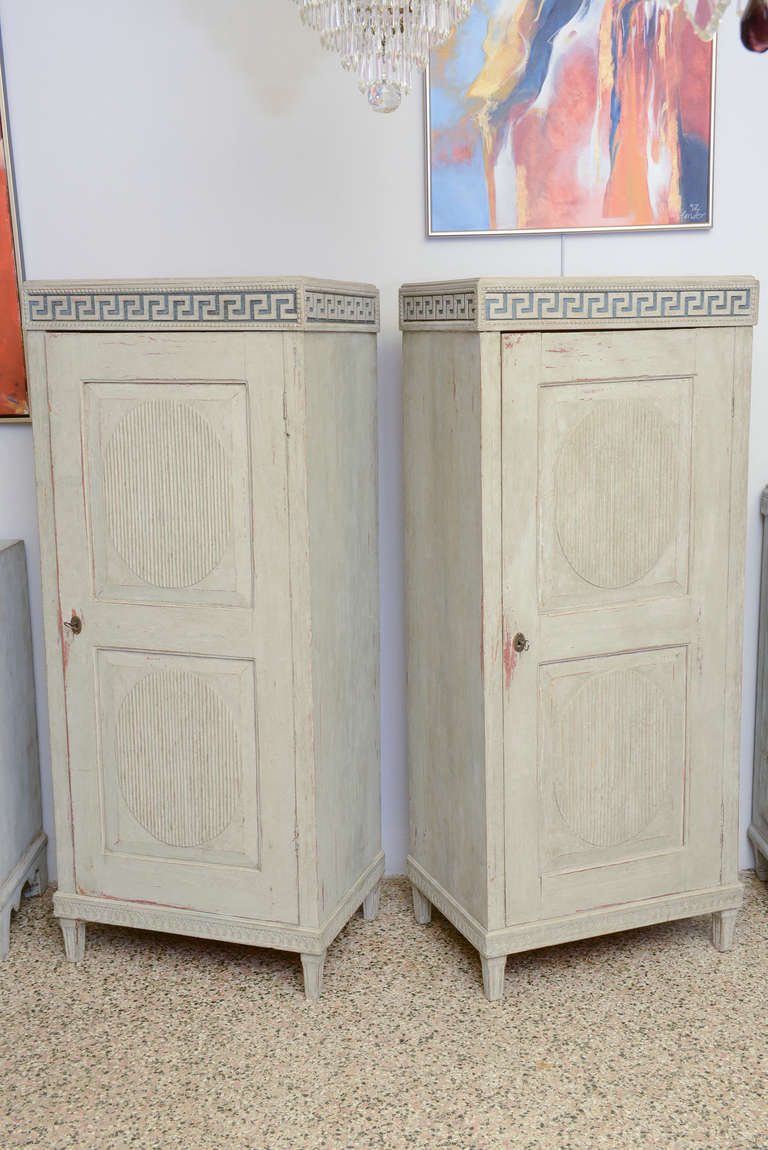 Beautiful pair of Gustavian cabinets have a neoclassic Greek key design carved at the top surrounded by a beaded edge. The raised panel doors each have two fluted oval designs and there is a carved lamb's tongue design on the lower cabinet edge just