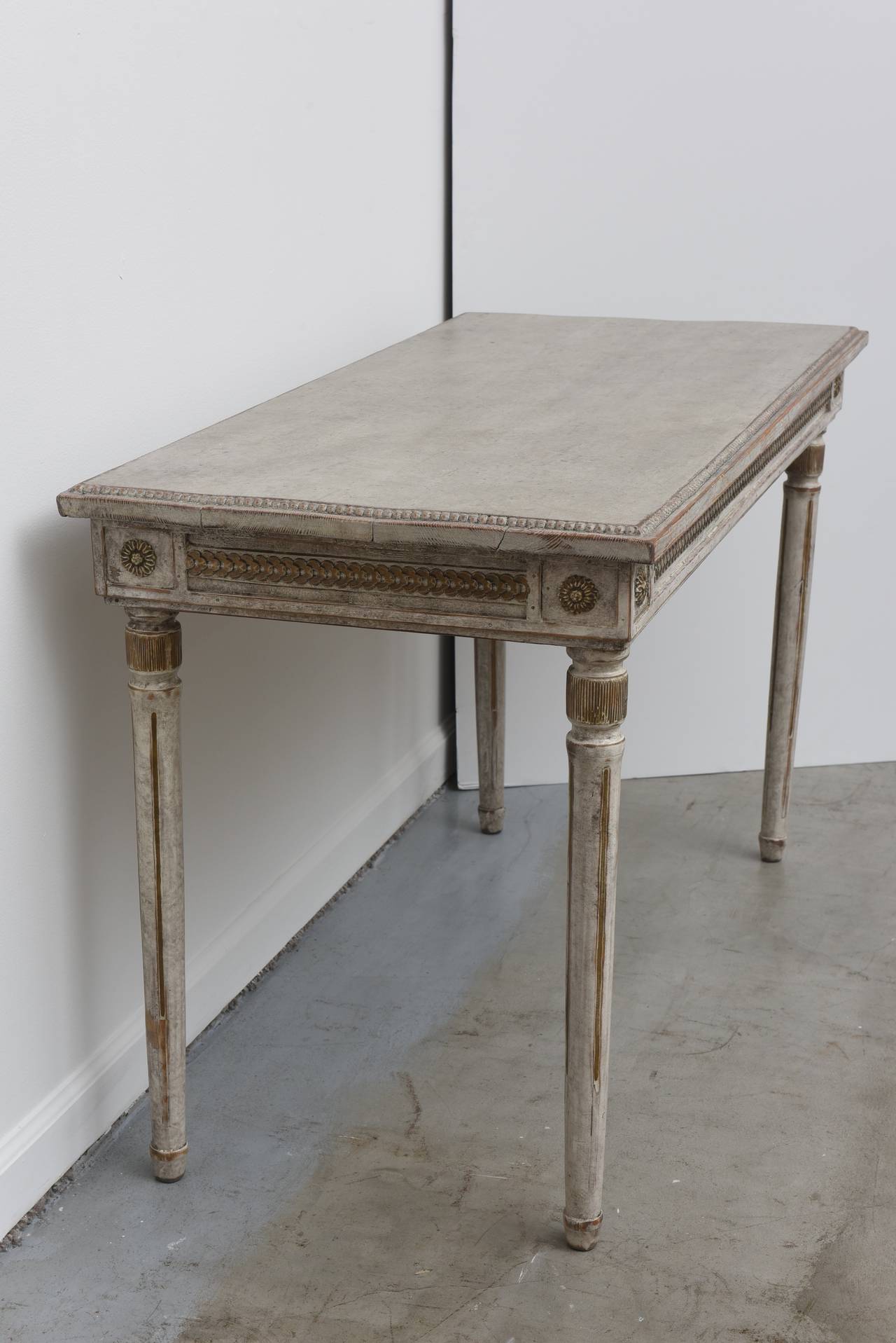 Painted Antique Swedish Console Table, Mid-19th Century. A carved beaded top sets off the apron below, which features a carved chain design with inset carved rosettes at each corner. An exquisitely carved rondel sits near the top of each tapered