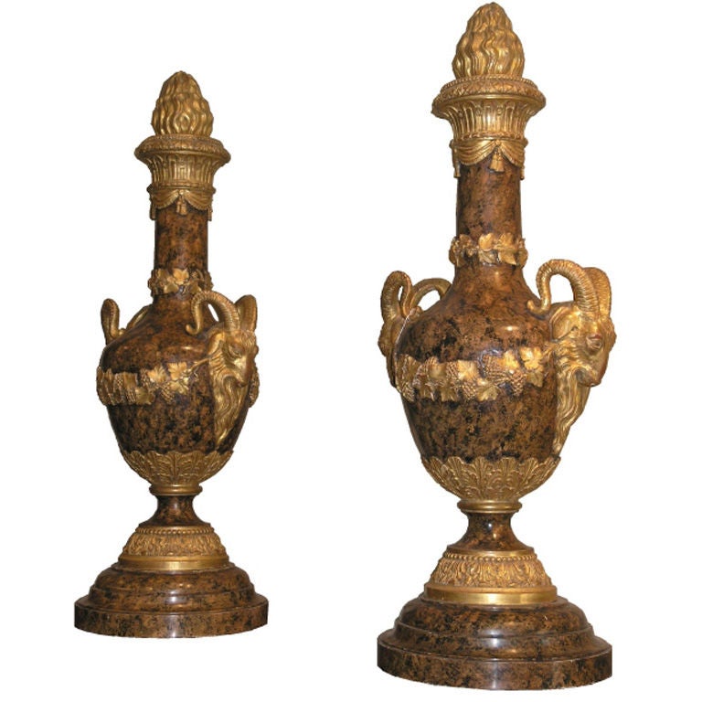 Fine pair of Italian giltwood and faux marble urns. Each with a flaming giltwood final above fluted neck, the bodies decorated with grape and vine leaves flanked by bold rams heads on turned leaf tip socle and circular plinth base.