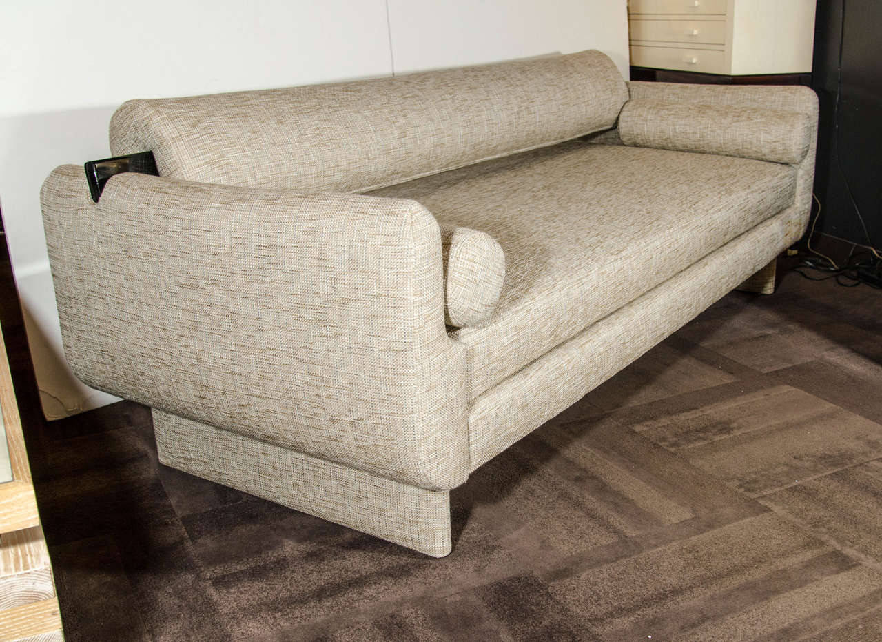 Sleek all upholstered sofa with streamline design.  Newly upholstered in a fine woven tweed fabric in hues of ecru, ivory, and khaki.  The sofa features beautiful ebonized wood handles on the long back bolster, and easily converts into a daybed or