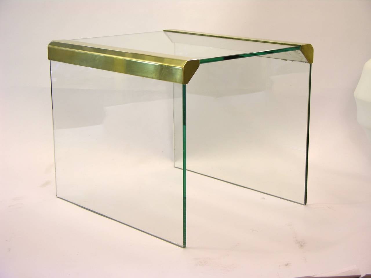 A very elegant and practical pair of side low tables designed by Pierangelo Gallotti for Gallotti & Radice. High quality of manufacturing: the clear tempered glass, 0.3 inch thick, has exquisite bevelled edges, the brass borders enhanced by a cut