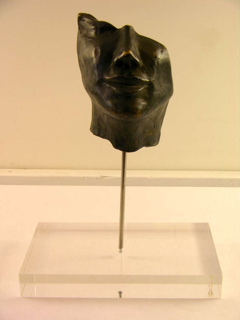 Diese hohle Bronzeskulptur des italienischen Künstlers Ginestroni vom Ende des 20. Jahrhunderts stellt einen Teil eines Gesichts dar:: das unsere Phantasie den Raum ausfüllen lässt. 
Die Montage der Skulptur auf einem Sockel aus Lucit ist eine