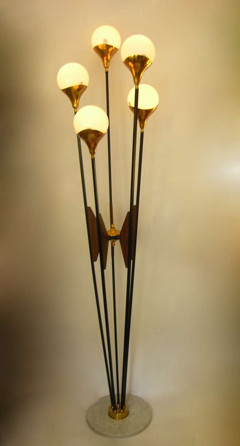 This floor lamp by Stilnovo, from the 1950s in original condition, is a model more sophisticated for the wooden motif linking together every metal pole to a central brass decoration with top and bottom finials.
It has 5 lights inside opaline glass