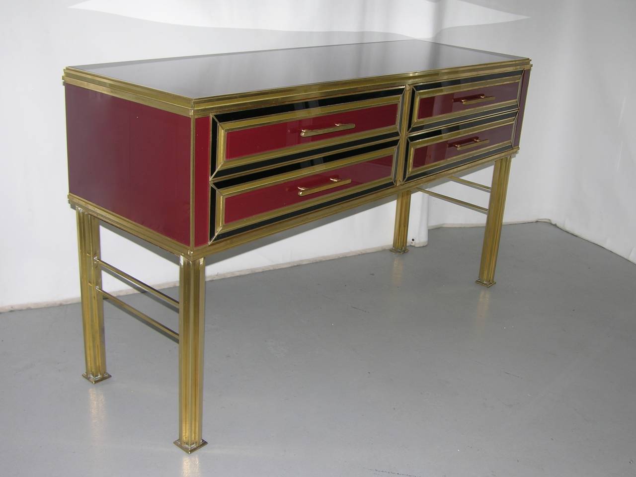 Late 1970s refined one of a kind Italian chest or console with four drawers of superb design, entirely hand manufactured, the wood structure covered in glass with a rare wine color, raised on exceptionally handcrafted stepped bronze legs with