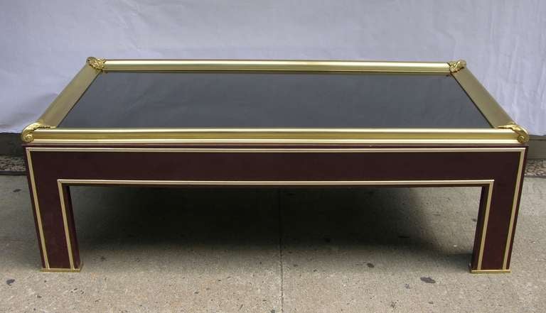 A very elegant Jansen coffee table of excellent design, the smoked mirrored top encased in a brass frame accented with bronze leaf moldings at each corner, the base lacquered in a rare deep burgundy with brass trims, on square angled feet.