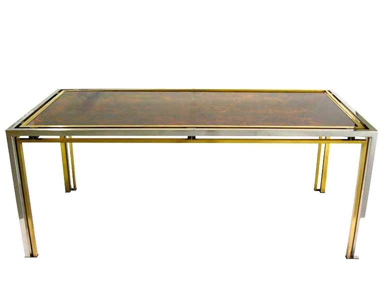 A superb table by Romeo Rega, very elegant with sophisticated Design and clean lines, the floating glass top is a magnificent Work of Art painted with reverse decor of gold leaf inclusions and lacquer and is encased in a brass and chrome double