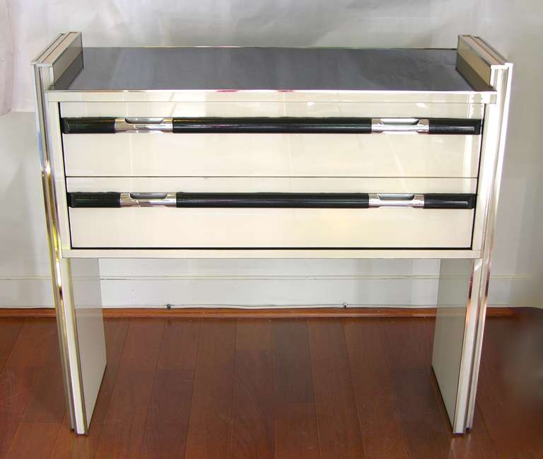 This is a very chic vintage small console/side table with two drawers, entirely edged with chromed metal lines, the surround is all black and ivory white glass. The design is extremely attractive and interesting as the central body looks suspended