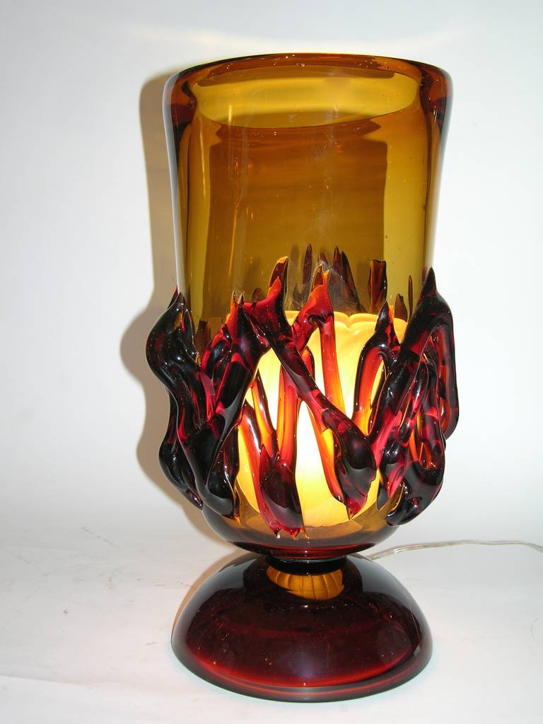 Atypical oval shaped pair of blown Murano glass lamps in a striking singular flamed amber color, decorated with free 3D blown applications in relief that give a rare dynamic effect and movement of flames. The light is intensified by an original oval