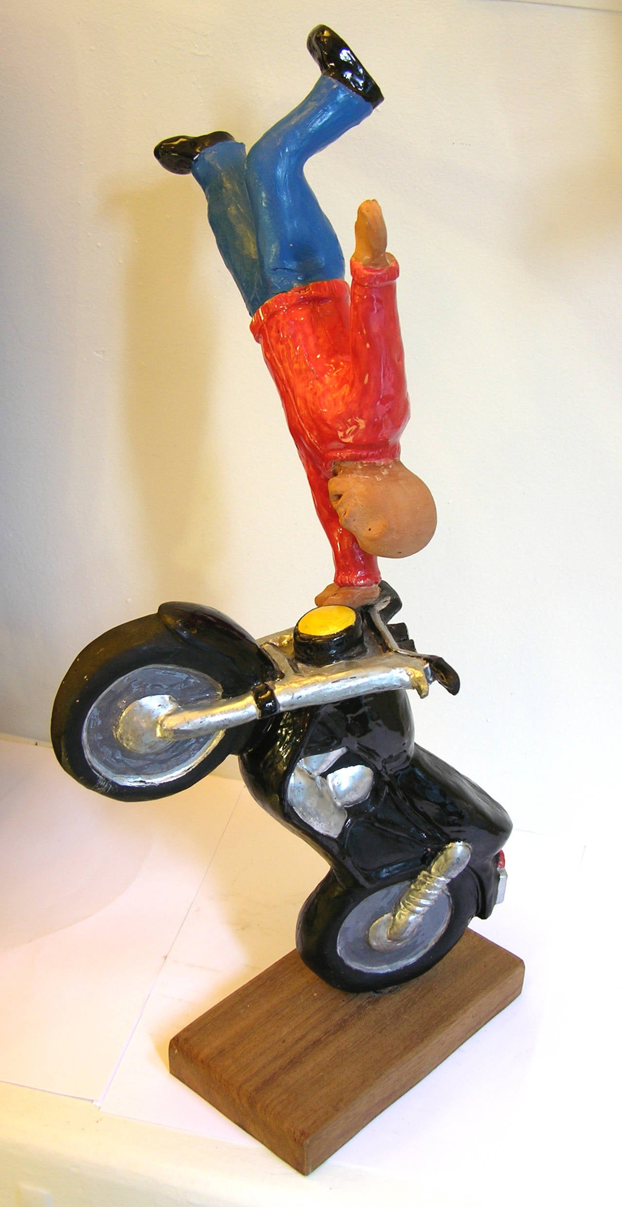 Handmade in terra cotta, this acrobat is performing a one hand stand on top of a motorcycle. This sculpture is hand-painted and fire enameled to enhance the detailed and precise design skillfully handcrafted. 
The sculpture is a very limited signed