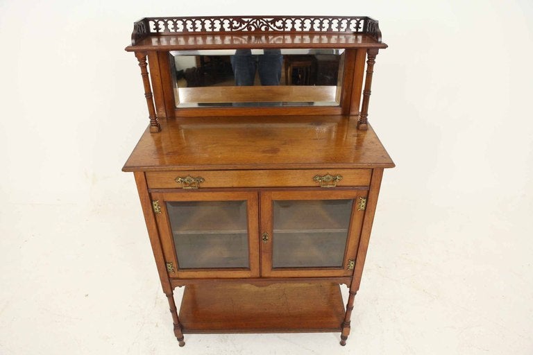 Petite Victorian mahogany two-door display / curio cabinet, fretwork gallery above bevelled mirror, single drawer above two (2) bevelled glass doors enclosing a single shelf above open shelf below, ending on turned legs.

Counter height is