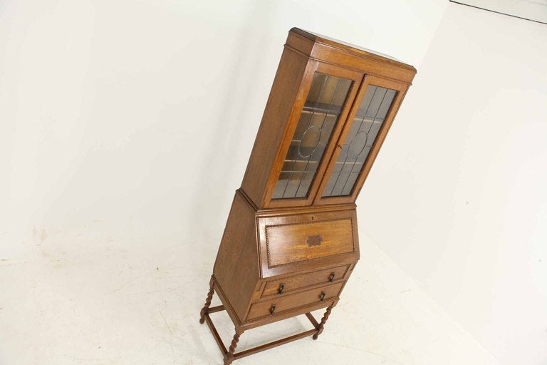 Oak barley twist leaded glass slant front desk with bookcase top, the rectangular top above two (2) leaded glass doors enclosing two (2) shelves above fall front with fitted interior, above two (2) drawers below, ending on barley twist legs