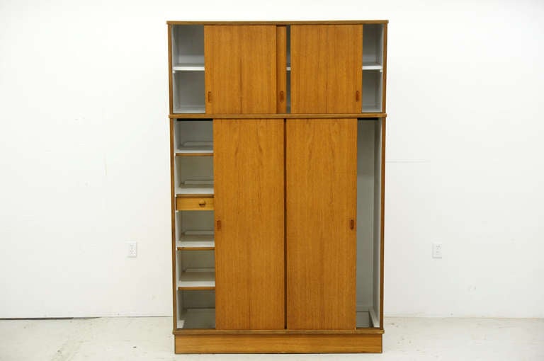 Nice three door teak wardrobe, dating to the 60′s. The doors open nicely and its very clean inside. Three sliding doors above opens to a single shelf inside each door. Below three sliding doors open to a hanging rod on either side. The left side
