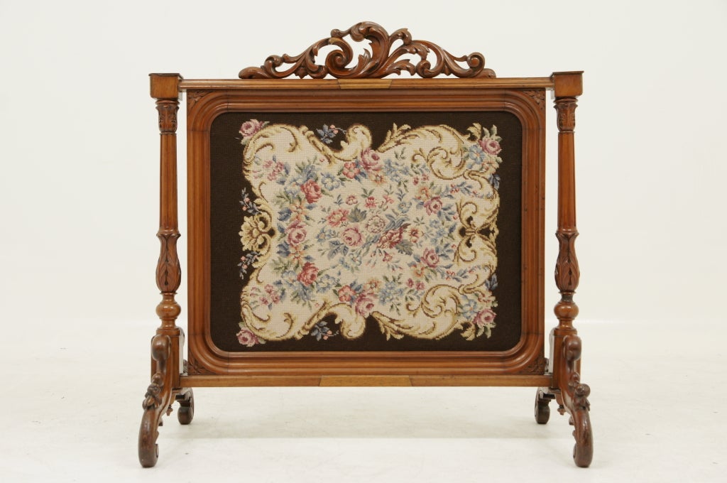 Ornately carved mahogany fire screen with an original needlepoint in carved frame supported by turned columns ending on carved feet.