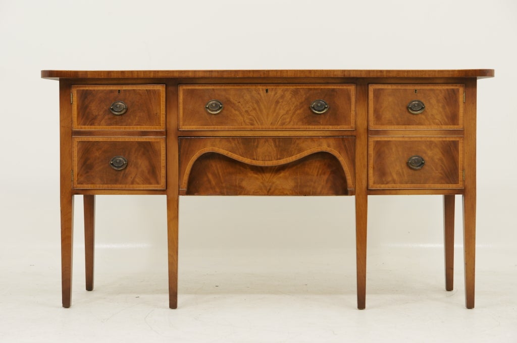 Inlaid mahogany serpentine sideboard, the cross banded top over a frieze and knee hole drawer flanked by cabinets, raised on fluted square tapering legs on pad feet.