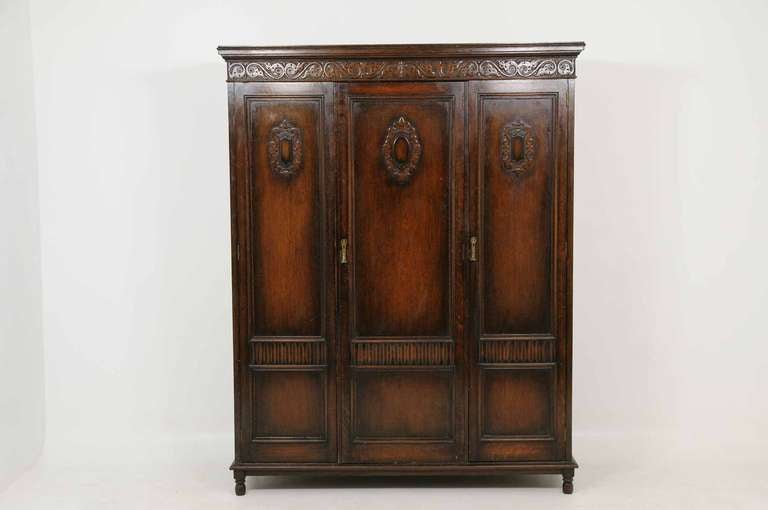 Early 20th century oak triple door armoire, the projected moulded top, carved cornice over three (3) panelled doors enclosing hanging space, full length mirror, three (3) open shelves, raised on plain base, ending on short turned feet.  Maker's
