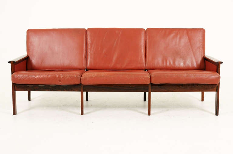Stunning rosewood and leather sofa designed by Illum Wikkelso¸ and manufactured by N. Eilersen. With its straightforward and minimal form and unique armrest joint, which is completely visible is the highlight of the design. The orangey red leather