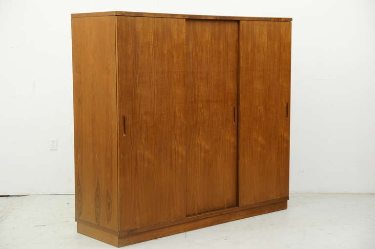 Nice three door teak wardrobe, dating to the 60”²s. The doors open nicely and its very clean inside. The right sliding door opens to five shelves and a single drawer which are all removable. The left side and center sliding doors open to a hanging