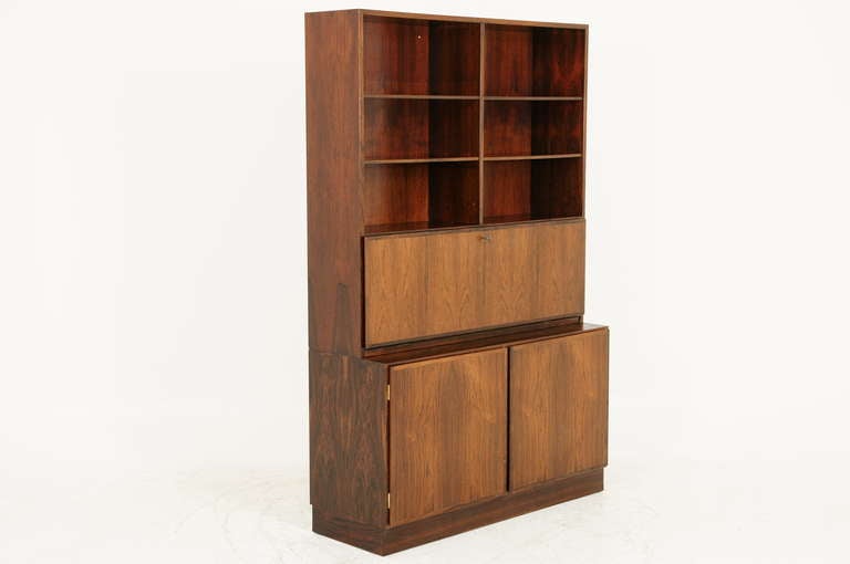 Two piece rosewood cabinet bookcase dating to the late 60's to early 70's by Omann Jun Mobelfabrik. Excellent quality piece with adjustable shelving above and two cupboard doors that open with lots of storage below. In the middle is a drop front