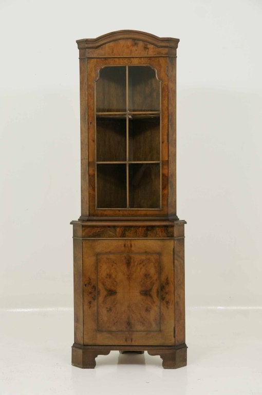 Burled walnut corner china cabinet with moulded cornice above single glazed door enclosing two (2) adjustable shelves above solid single door ending on shaped feet.