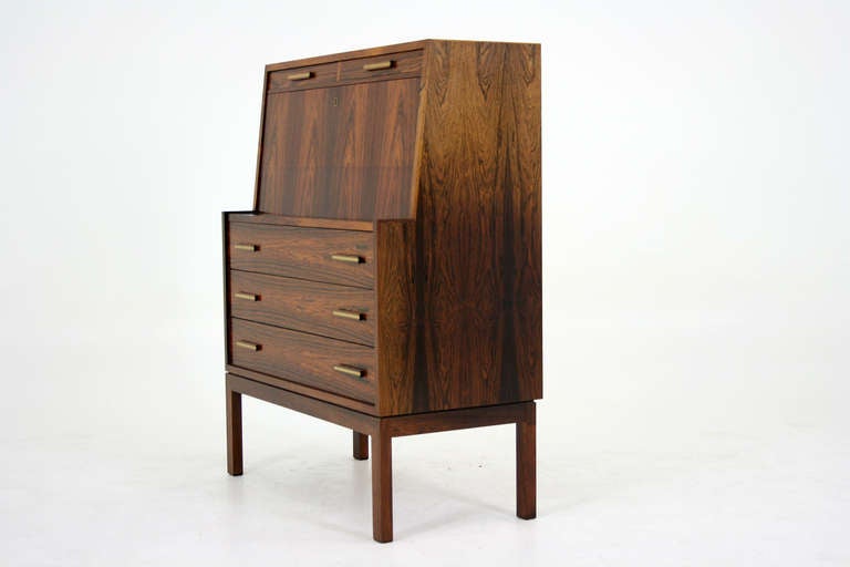 Gorgeous drop front desk or bureau in rosewood with brass trim, dating to the 60”²s. Fall front lid open to large work space with three small drawers and an open shelf inside. Two small drawers above and three drawers sit below the writing surface