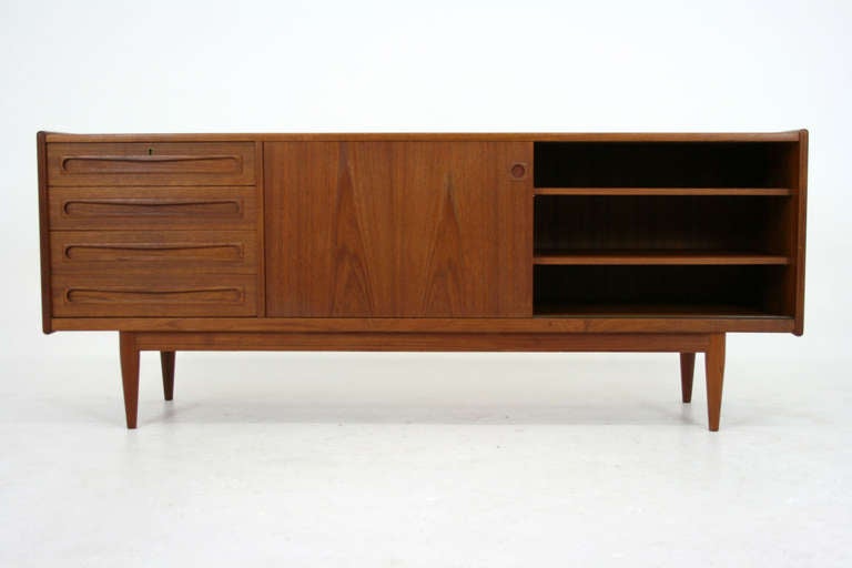 Nice danish teak sideboard dating to the 60's. Sideboard shows two sliding doors, which opens to two adjustable shelves on the right and one adjustable shelf on the left. Four drawers sit on the left. Top drawer has an extra sliding liner inside.