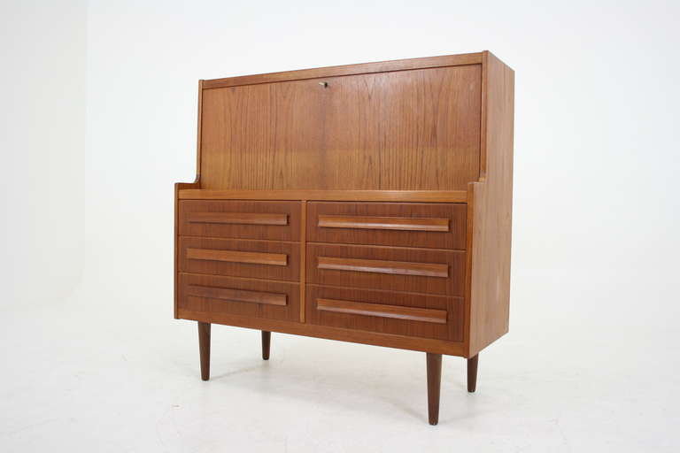 Beautiful drop front desk or bureau in teak, dating to the 60s. Fall front lid opens to large work space with two drawers and an open shelf inside in the center and two sliding doors that open up to reveal a single shelf inside. Six decent sized
