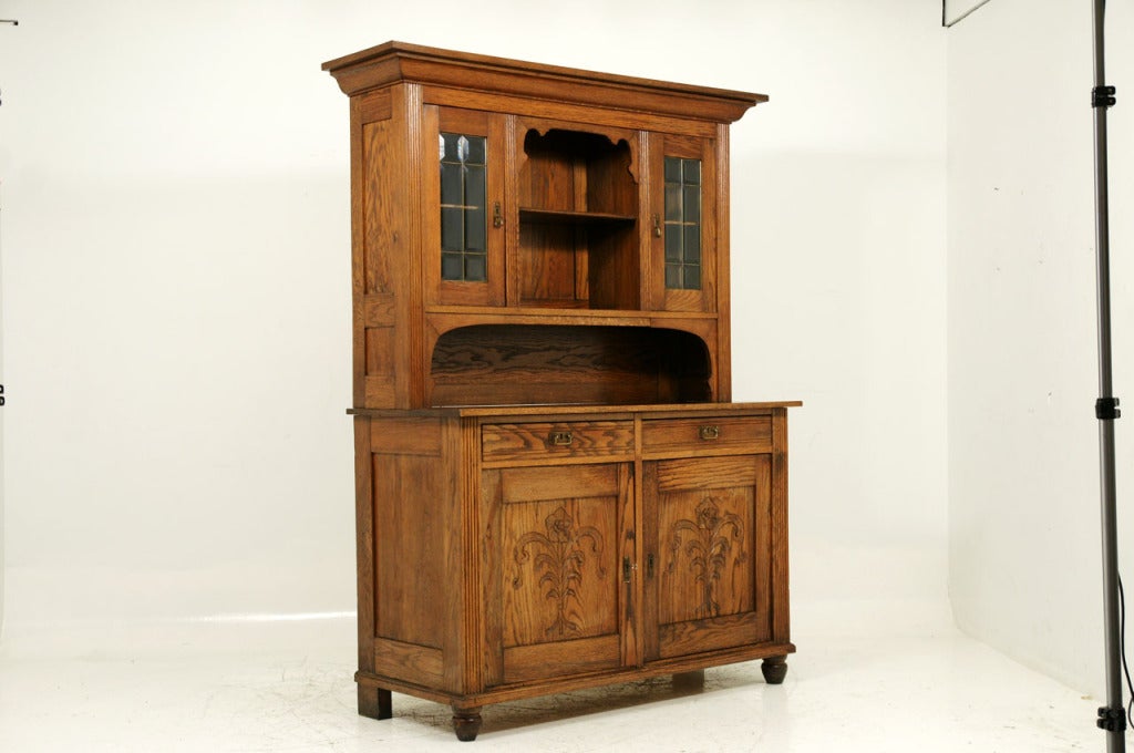 Large antique Danish oak buffet with a hutch top that has central open space flanked by two (2) bevelled glass cabinets above rectangular top, above two (2) sliding drawers, above two (2) carved doors enclosing shelves, raised on turned bun feet.
