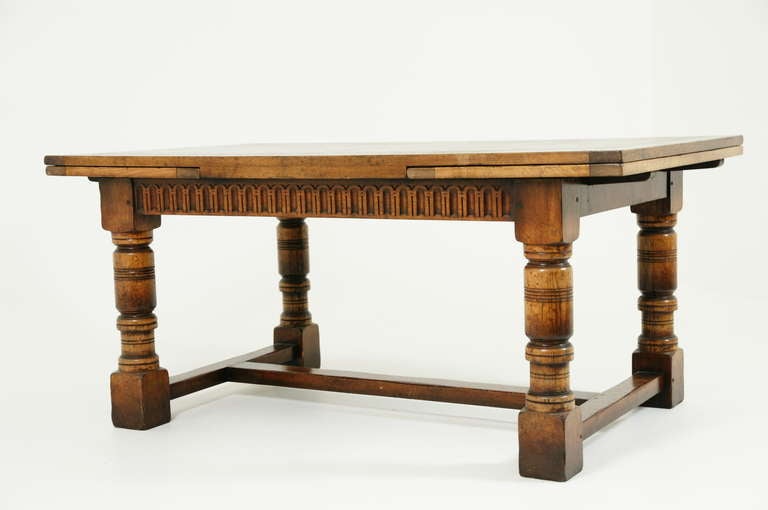 Large oak extending draw leaf dining, boardroom table. Rectangular top with pull out leaf on either end above carved apron.  Sitting on four large turned legs connected by cross stretchers.