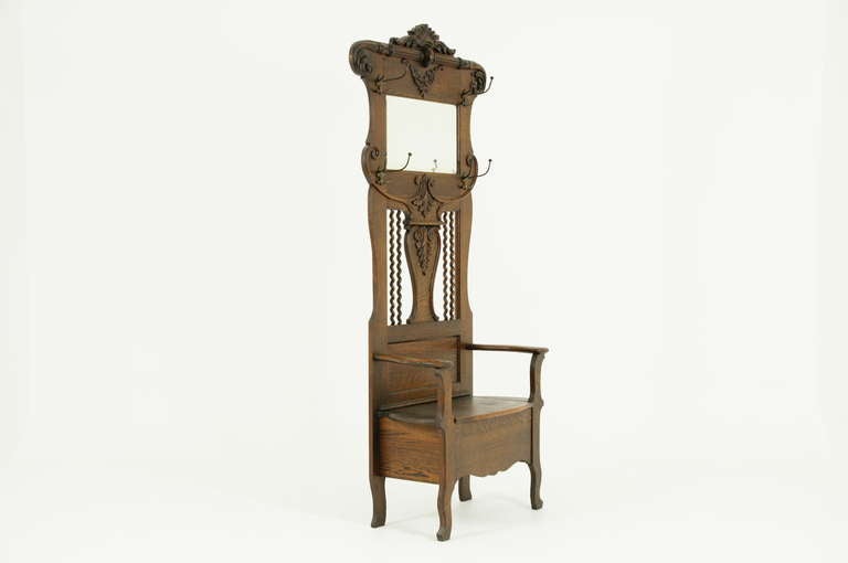 An early 20th Century Carved Oak Hall Tree with lift-up seat, shaped bevelled mirror and four sets of brass coat hooks.
