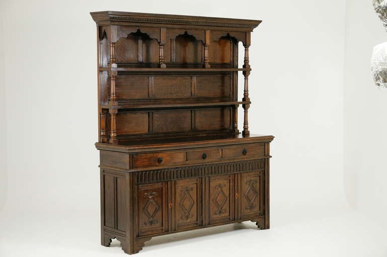 An impressive Oak Welsh Dresser with an Arts & Crafts design.  The projected carved cornice above two open shelves held-up by turned supports and moulded rectangular top.  Three drawers above four carved doors fitted with single shelf and slide-out