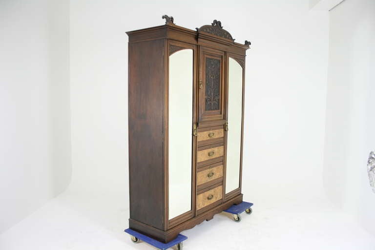 A superb Art Nouveau Triple Door Armoire Wardrobe with carved pediment top, moulded cornice above central carved door, four long drawers below, flanked by two full length mirrored doors enclosing shelf with hanging space, brass hooks, ending on a