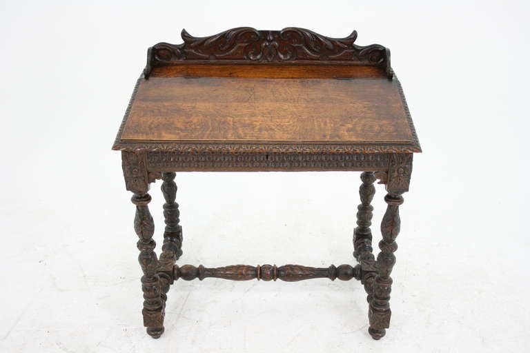 A late Victorian carved oak lift top, slant writing table with three-quarter gallery above slant front with fitted interior carved sides and front supported by heavily carved supports ending on carved feet with ornate turned cross-stretcher.