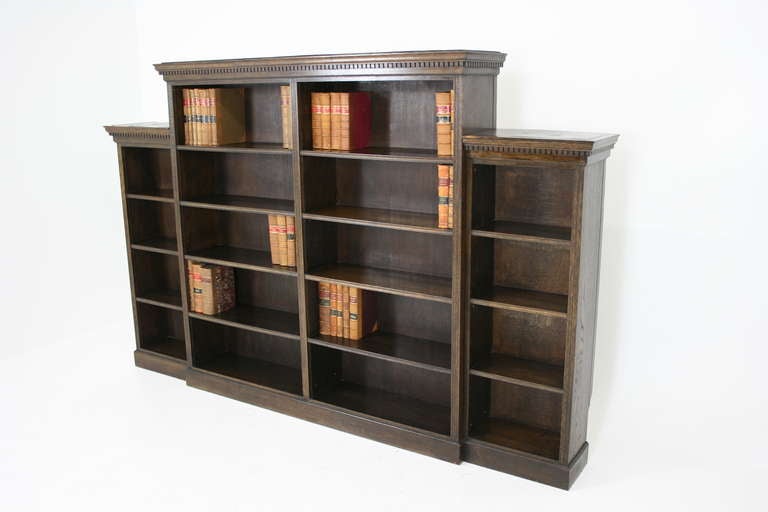 An early 20th Century Oak Open Bookcase with rectangular top, dentil cornice with eight fixed wooden shelves flanked by two shorter bookcases with six fixed wooden shelves, ending on a plinth base.