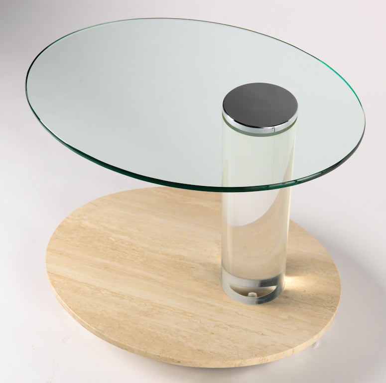 La table d'appoint ovale a un plateau en verre avec un capuchon rond chromé, une colonne en lucite, une tablette inférieure en travertin et une base en métal. Roues en dessous pour faciliter le déplacement dans l'espace de vie/de travail. 