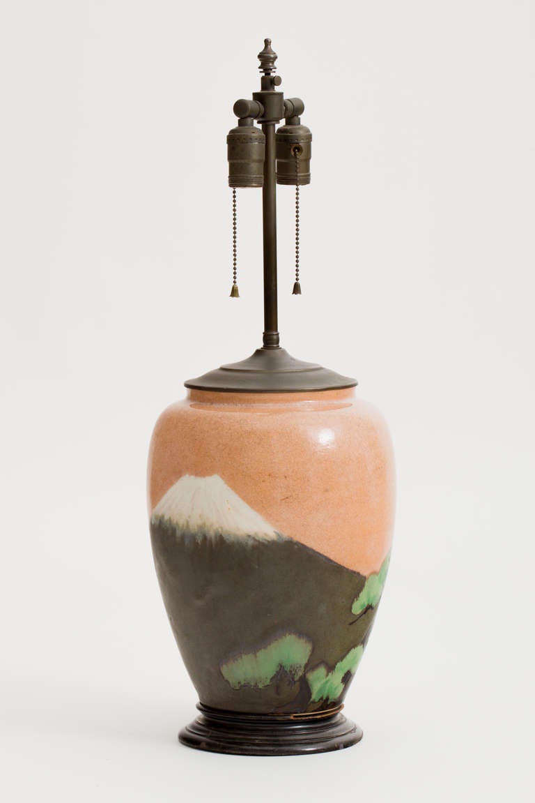 Lovely matte glaze Arts and Crafts pottery lamp with Mount Fuji motif. The design is unique all the way around the lamp in colors of pale peach, matte dark gray, green and white. Signed with hallmark on ceramic lamp bottom, pictured.  Wood base