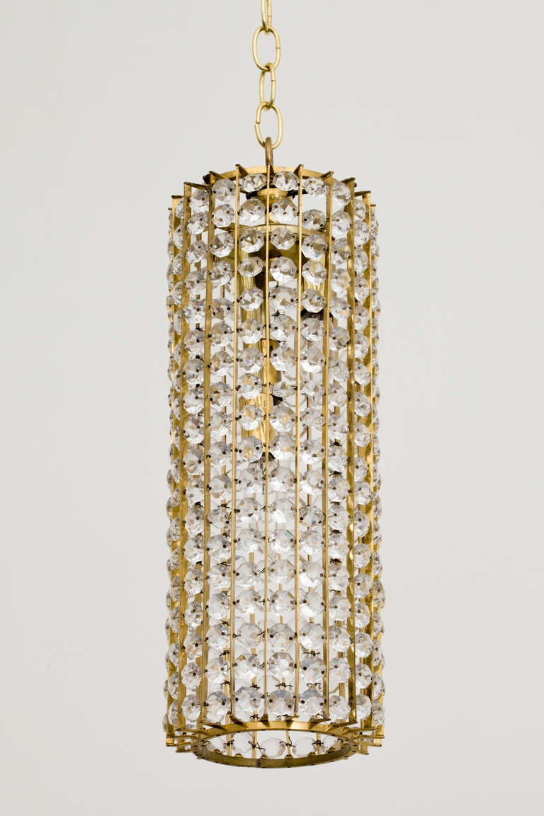 Large cylindrical brass and faceted crystal chandelier hangs with round brass ceiling cap and chain, circa 1960. The chandelier body measures 18 inches height, and has 360 crystals total, for beautiful illumination. Three sockets, 60 max wattage