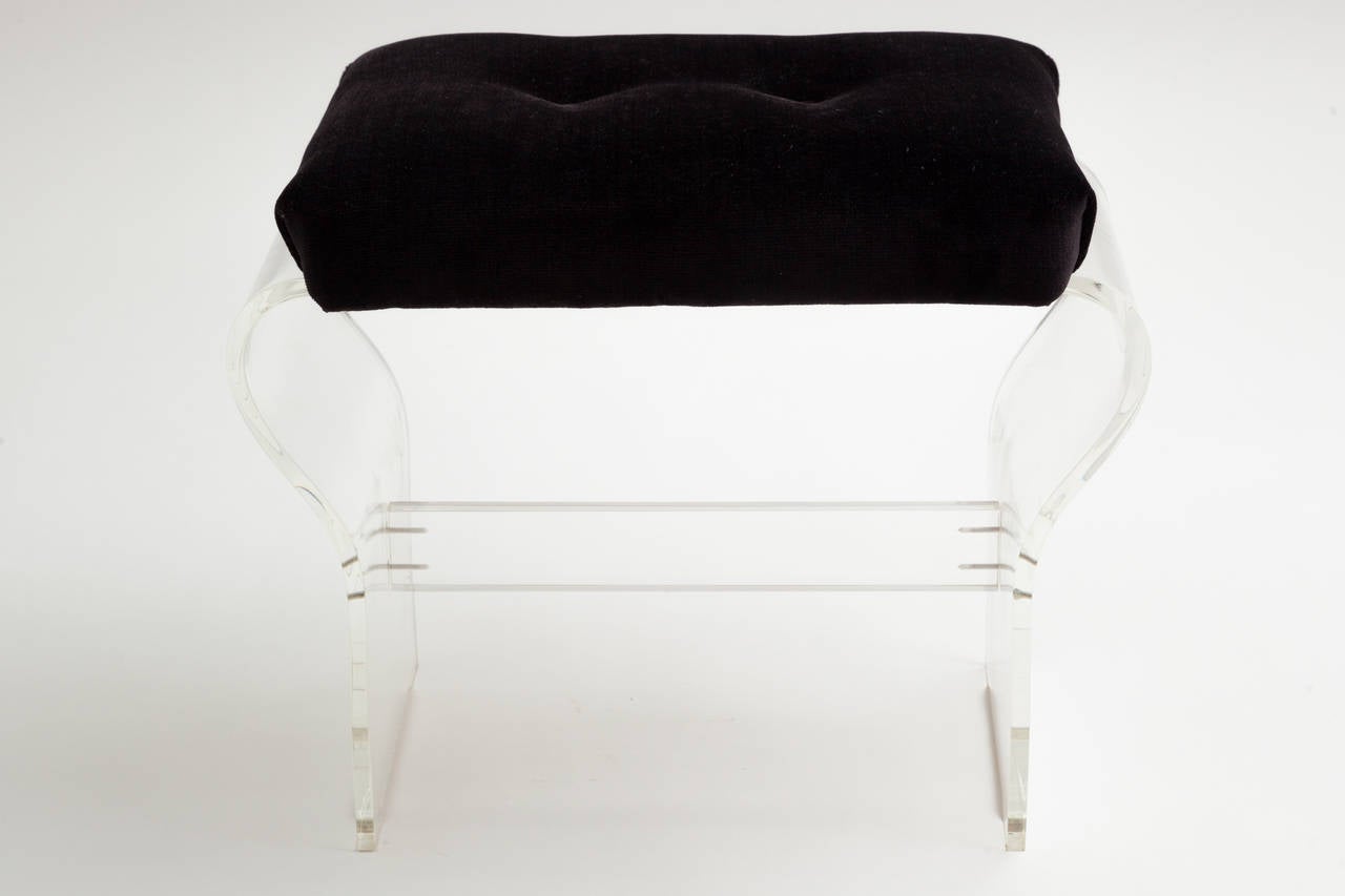 Lucite ottoman bench with curved sides and black velvet upholstery, circa 1970s. Upholstered seat cushion measures 18" width x 4.5" depth.