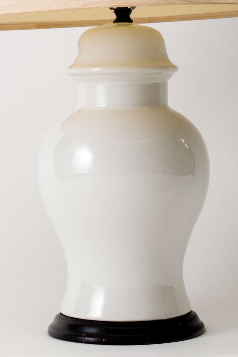 Pair of white ceramic ginger jar lamps mounted on circular ebonized wood bases, circa 1960.
