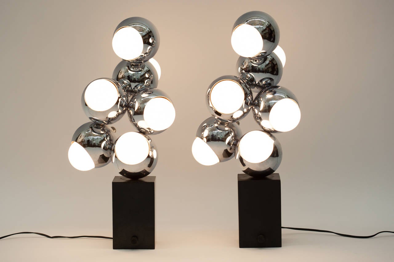 Pair of chrome atomic cluster lamps on black pedestal bases. Six globes per lamp. Light may be adjusted with switch. Light bulbs not included.