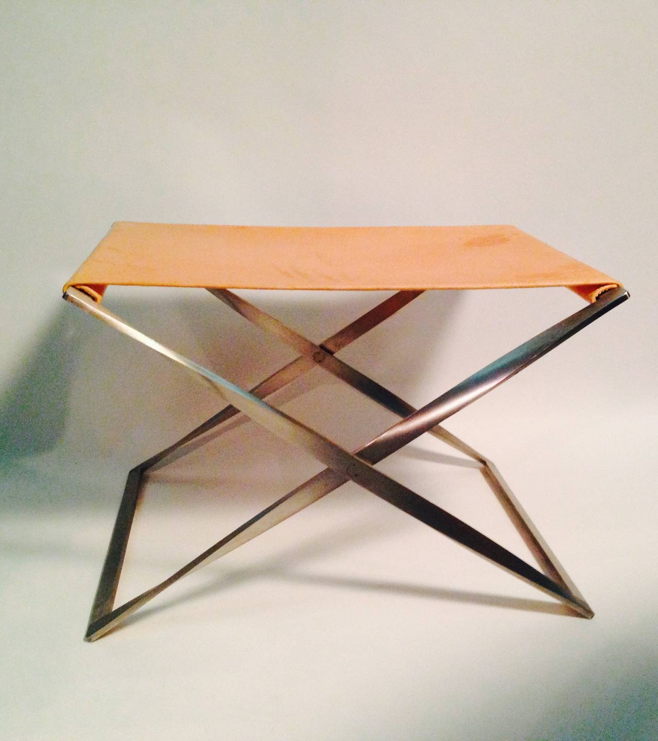 Folding steel with leather stool designed by Poul Kjærholm. Elegant stainless steel legs with pale cognac color leather seat. Designed in the 1960s.