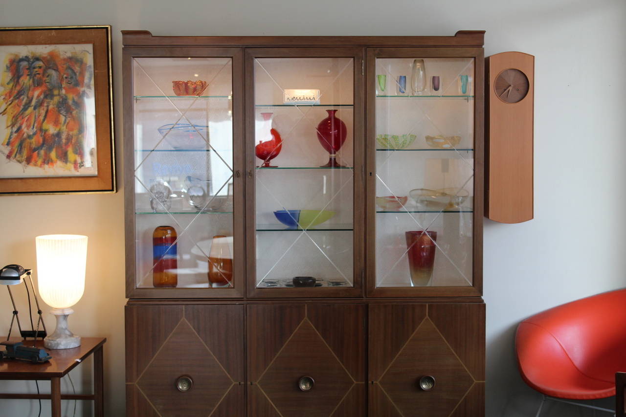 Lovely two-piece cabinet designed by Tommi Parzinger for Charak, circa 1948. Lower portion of the cabinet features three diamond inlay doors with brass pulls. Each side has two adjustable wood shelves; center door has five drawers (pictured). The