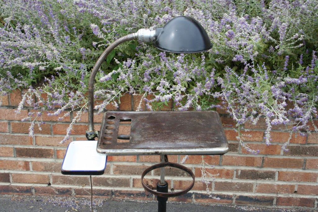 A super unique industrial tray table, originally designed for a dentist.  The table is on a swag leg base with rollers and adjusts in height by a tension knob on the side.  Tray has two attachments, one is a small enameled metal tray and the other