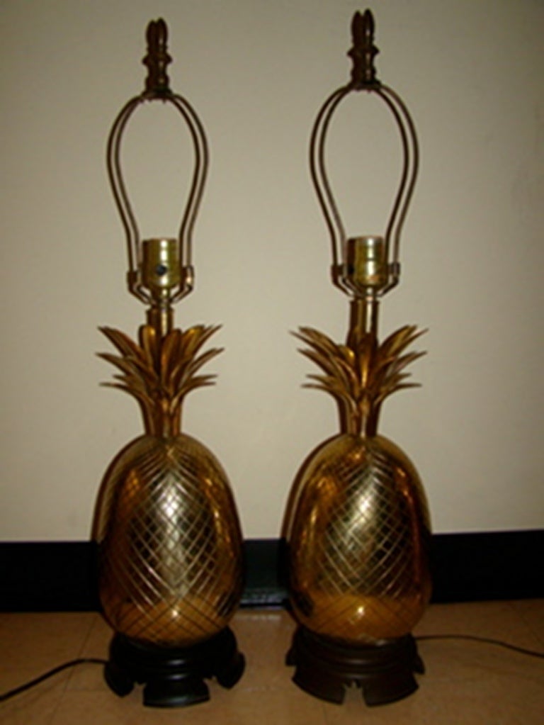 Elegant pair of Large matching Brass Pineapple Table Lamps. Comprised of sculptural solid brass in the form of Pineapples. Each rest of a carved wood base with matching finials. Pineapples measure 14